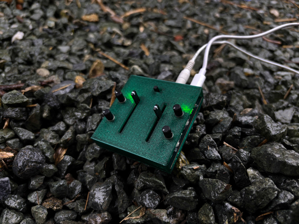A photo of Lore, a small green synthesizer made of bioplastic, on rocks